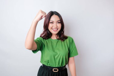 Mutlu ve başarılı bir ifadeyle genç bir Asyalı kadın yeşil gömlek giyiyor beyaz arka planda izole edilmiş.