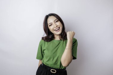 Mutlu ve başarılı bir ifadeyle genç bir Asyalı kadın yeşil gömlek giyiyor beyaz arka planda izole edilmiş.