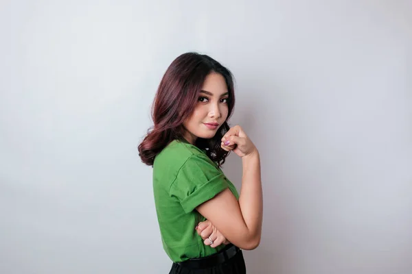 興奮したアジアの女性は 彼女の腕と筋肉を誇らしげに笑顔持ち上げることによって強いジェスチャーを示す緑のTシャツを着て — ストック写真
