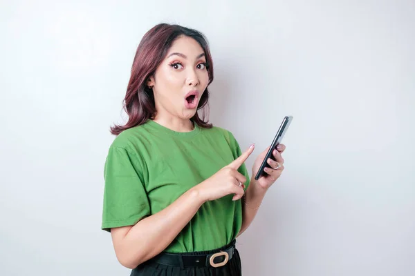 Έκπληκτη Ασιάτισσα Που Φοράει Πράσινο Μπλουζάκι Δείχνοντας Smartphone Της Απομονωμένη — Φωτογραφία Αρχείου