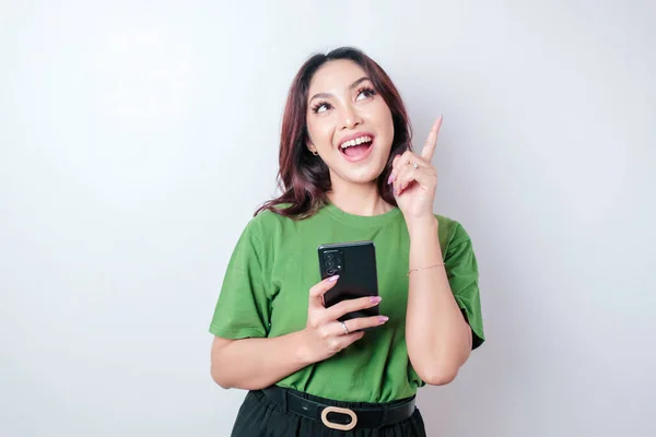 Посмішка Красива Азіатка Вказує Пальцем Вгору Порожній Простір Тримаючи Телефон — стокове фото