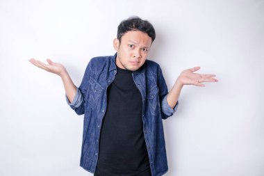 Omuzlarını silkeleyen lacivert tişörtlü Asyalı bir adamın portresi çok şaşkın görünüyor, beyaz bir arka planla izole edilmiş.