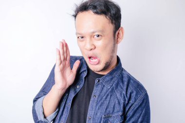 Asyalı genç adam lacivert gömlek giyiyor, ağızdan ağıza konuşuyor, gizli söylentiler yayıyor, kötü niyetli konuşmalar fısıldıyor.