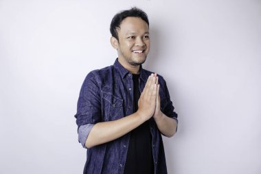 Gülümseyen Asyalı genç adam beyaz arka planda izole edilmiş geleneksel selamlaşmaları işaret ediyor.
