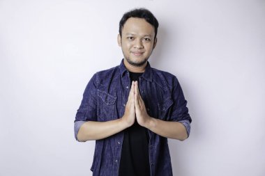 Gülümseyen Asyalı genç adam beyaz arka planda izole edilmiş geleneksel selamlaşmaları işaret ediyor.