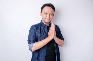 Gülümseyen Asyalı genç adam beyaz arka planda izole edilmiş geleneksel selamlaşmaları işaret ediyor.