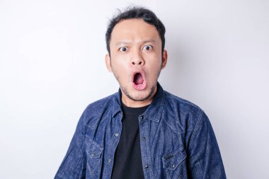 Şok olmuş Asyalı bir adamın portresi, lacivert gömlek giyiyor, beyaz bir arka planla izole edilmiş.
