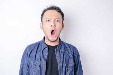 Şok olmuş Asyalı bir adamın portresi, lacivert gömlek giyiyor, beyaz bir arka planla izole edilmiş.