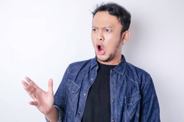 Şok olmuş Asyalı bir adamın portresi, lacivert gömlek giyiyor, beyaz bir arka planla izole edilmiş.
