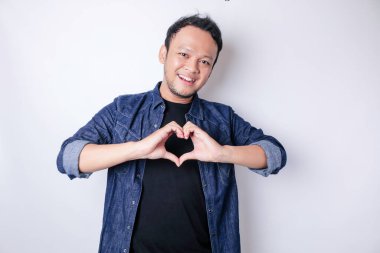 Lacivert tişört giyen çekici bir Asyalı genç adam mutlu olur ve romantik şekilli bir kalp hareketi şefkatli duygular ifade eder.