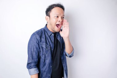 Mavi bir donanma gömleği giyen genç ve güzel bir adam ağzında bir eliyle bağırıyor ve çığlık atıyordu. iletişim konsepti.