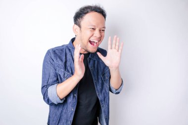 Mavi bir donanma gömleği giyen genç ve güzel bir adam ağzında bir eliyle bağırıyor ve çığlık atıyordu. iletişim konsepti.