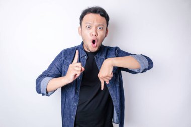 Şok olmuş Asyalı adam mavi donanma tişörtü giymiş. Alttaki ve üstteki fotokopi alanını işaret ediyor. Beyaz arka planla izole edilmiş.