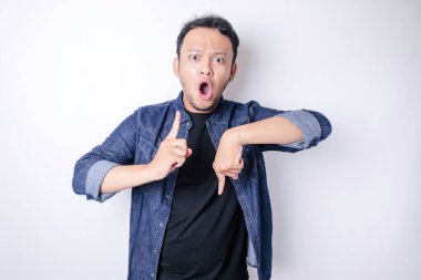 Şok olmuş Asyalı adam mavi donanma tişörtü giymiş. Alttaki ve üstteki fotokopi alanını işaret ediyor. Beyaz arka planla izole edilmiş.