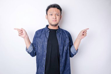 Kafası karışmış, lacivert gömlekli bir adam yanındaki fotokopi alanını işaret ediyor, beyaz bir arka planla izole edilmiş.