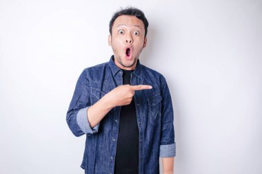 Şok olmuş Asyalı adam mavi donanma tişörtü giymiş, yanındaki fotokopi alanını işaret ediyor, beyaz arka planla izole edilmiş.