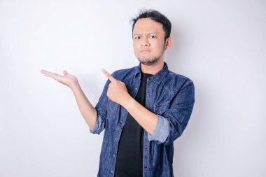 Kafası karışmış, lacivert gömlekli bir adam yanındaki fotokopi alanını işaret ediyor, beyaz bir arka planla izole edilmiş.