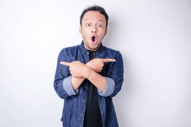 Şok olmuş Asyalı adam mavi donanma tişörtü giymiş, yanındaki fotokopi alanını işaret ediyor, beyaz arka planla izole edilmiş.