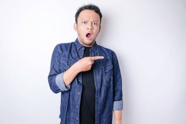 Şok olmuş Asyalı adam mavi donanma tişörtü giymiş, yanındaki fotokopi alanını işaret ediyor, beyaz arka planla izole edilmiş.