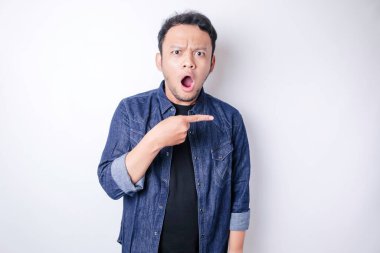 Şok olmuş Asyalı adam mavi donanma tişörtü giymiş, yanındaki fotokopi alanını işaret ediyor, beyaz arka planla izole edilmiş.