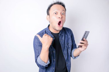 Donanma mavisi tişörtlü, beyaz arka planla izole edilmiş akıllı telefonunu işaret eden Asyalı bir adam.