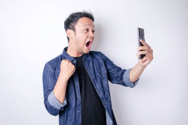Donanma mavisi tişörtlü, beyaz arka planla izole edilmiş akıllı telefonunu işaret eden Asyalı bir adam.