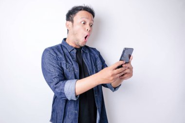 Donanma mavisi tişörtlü, beyaz arka planla izole edilmiş akıllı telefonunu işaret eden Asyalı bir adam.