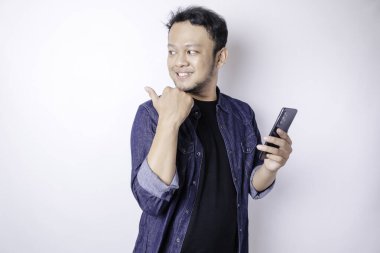 Gülümseyen yakışıklı Asyalı adam telefonunu izole edilmiş beyaz arka planda tutarken boş alanı işaret ediyor.