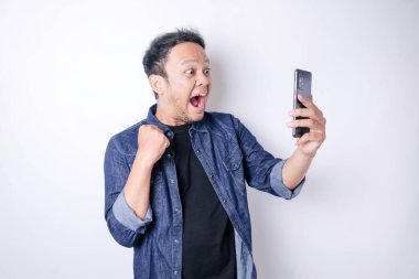 Mutlu bir yüzü olan, lacivert tişört giyen ve elinde beyaz arka planla izole edilmiş akıllı telefon tutan genç bir Asyalı.