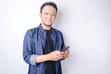 Gülümseyen Asyalı bir adamın portresi gülümsüyor ve elinde telefonuyla donanma mavisi bir gömlek giyiyor.