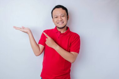 Gülümseyen güzel Asyalı adam, boş bir alanı işaret ediyor. Yanındaki izole beyaz arka plan.