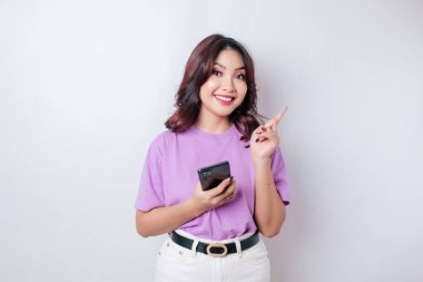 Gülümseyen Asyalı güzel bir kadın telefonunu izole edilmiş beyaz arka planda tutarken boş bir yeri işaret ediyor.