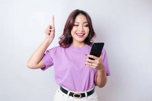 Uśmiechnięta Piękna Azjatka Wskazując Palcem Górę Pustej Przestrzeni Trzymając Telefon — Zdjęcie stockowe