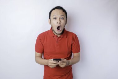 Kırmızı tişörtlü, beyaz arka planla izole edilmiş akıllı telefonunu işaret eden Asyalı bir adam.