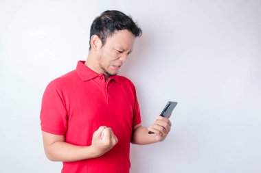 Mutlu bir yüzü olan, kırmızı tişörtlü ve elinde beyaz arka planla izole edilmiş akıllı telefonu tutan genç bir Asyalı.