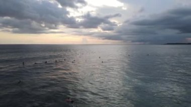 Bali, Endonezya 'da gün batımında dalgalarda sörf yapan insanların hava görüntüsü.
