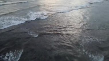 Bali, Endonezya 'da gün batımında dalgalarda sörf yapan insanların hava görüntüsü.