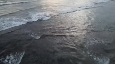 Bali, Endonezya 'da gün batımında dalgalarda sörf yapan insanların hava görüntüsü.