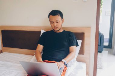 Yatakta dizüstü bilgisayarını kontrol ederken esneyen uykulu genç bir adam..