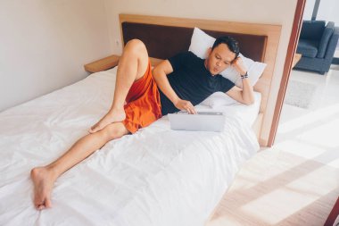 Yataktan çalışan gülümseyen genç adam. Dizüstü bilgisayara bakarken yalan söylüyor..