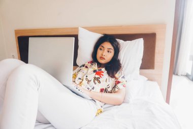 Yataktan çalışan konsantre olmuş genç bir kadın. Dizlerinin üzerine çök ve klavyeye yaz..