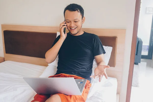 Jovem Feliz Trabalhar Cama Segure Laptop Joelhos Falando Telefone — Fotografia de Stock