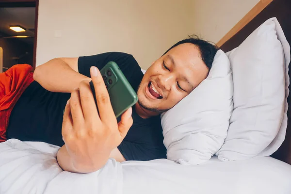 Smiling Indonesian Man Phone Bed Lying Side Relax — Stok Foto