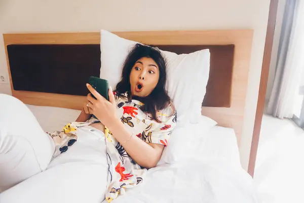 Шокированная Молодая Женщина Проверяет Телефон Пока Лежит Постели — стоковое фото