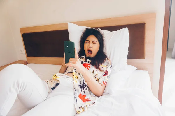 Сонная Молодая Женщина Зевает Держа Телефон Кровати — стоковое фото