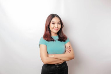 Mavi tişörtlü, kollarını kavuşturup beyaz arka planda izole edilmiş kameraya bakan kendinden emin gülümseyen Asyalı bir kadının portresi.