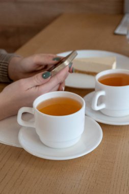 iki fincan çay ve bir cheesecake keki bir kızın elinde telefon, kafede öğle yemeği atıştırmalığı.