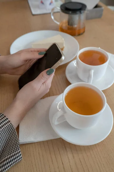 Twee kopjes thee en een kwarktaart een meisje hand met een telefoon in haar handen in een cafe daglicht lunch snack — Stockfoto