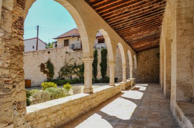 Kıbrıs Rum Kesimi, mimari, köy kilisesi, pitoresk konum, ortaçağ merkezi, yan kemerli galeriler, çan kulesi, taş döşemeler, apse, kiremitli çatı, taş döşeli avlu, uzun ağaçların gölgesi, yürüyüş, seyahat, turizm     