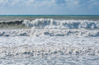 Güçlü bir Kasım rüzgarı, kıyıya doğru kükreyen dalgalar salıyor ve beyaz köpükleri kopartıyor. Paphos yakınlarındaki ünlü kumlu mercan plajı fırtınalı sularla doludur..   
